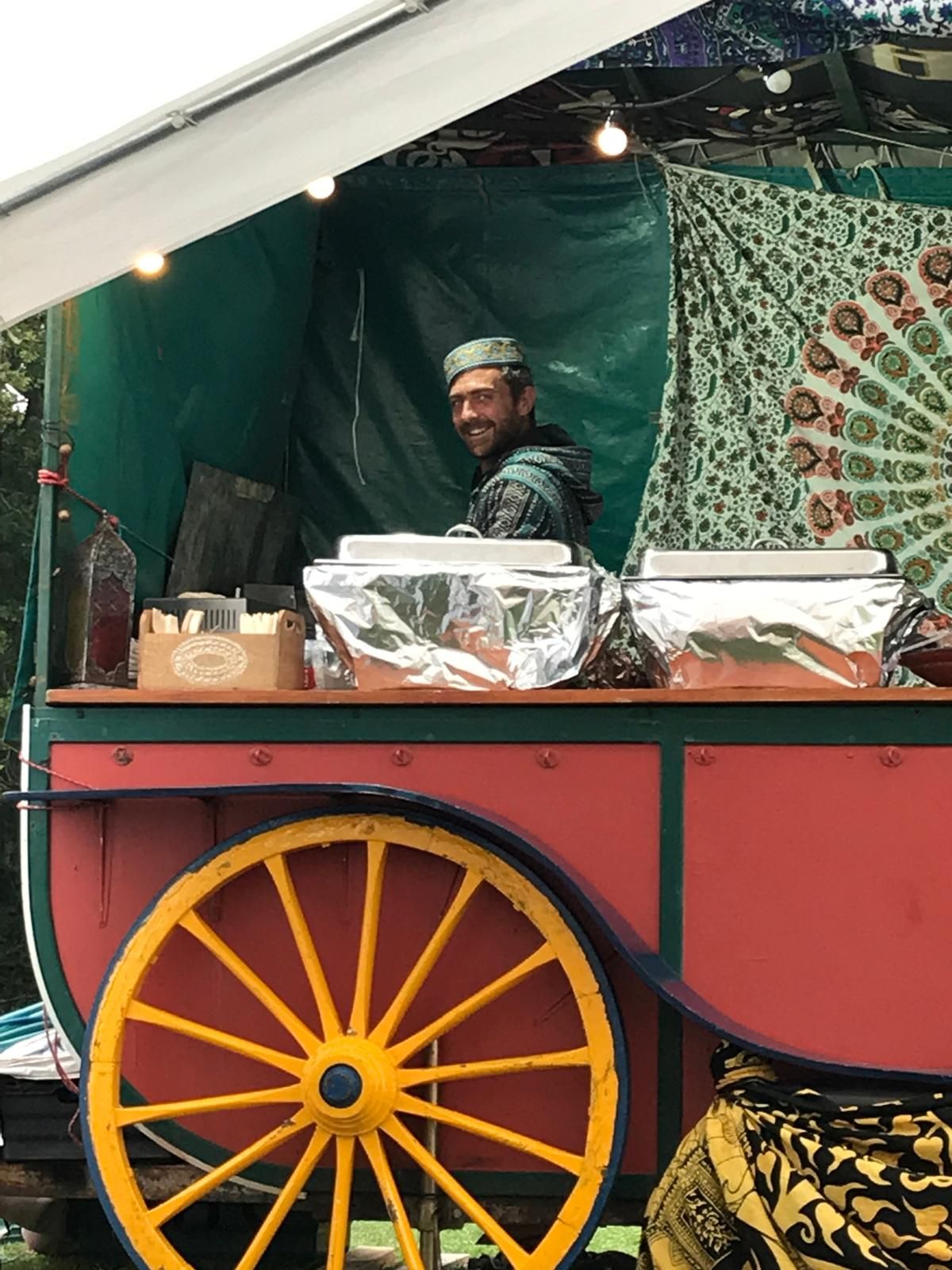Smiling behind the counter of the painted Falafel Shack wagon, under fairy lights